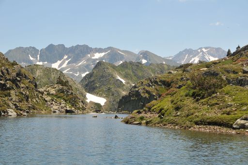 A beautiful view of a serene river surrounded by green hills and snowy peaks in the Catalan Pyrenees