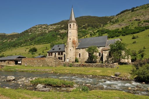 A river running through a lush green forest with a small church in the background