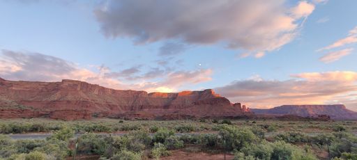 A panoramic view of a canyon covered with green trees and shrubs at sunset