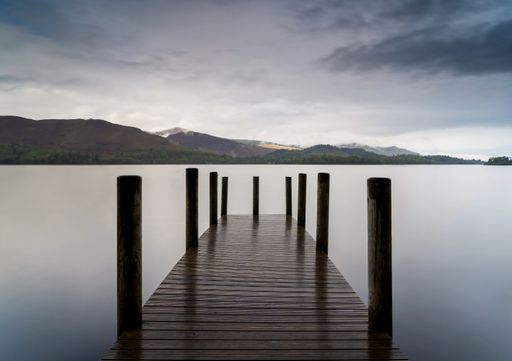 A wooden pier extending into a tranquil lake beneath a cloudy sky