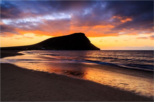 A beautiful shot of a bright sunset sky over a seashore with a cliff on Tenerife Island