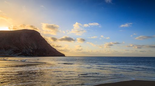 A beautiful shot of a bright sunset sky over a seashore with a cliff on Tenerife Island