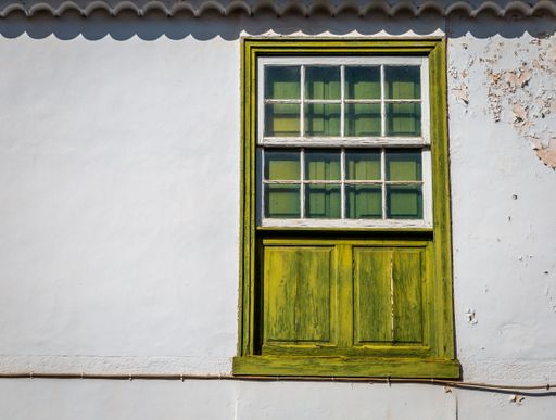 An old house wall with a window in a bright olive green frame. Costa Adeje, Tenerife, Spain.