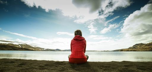 A panoramic shot of the female from behind sitting on the sandy beach and enjoying the view
