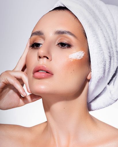 A vertical closeup shot of a beautiful female face showcasing skincare cream with her hair in a towel