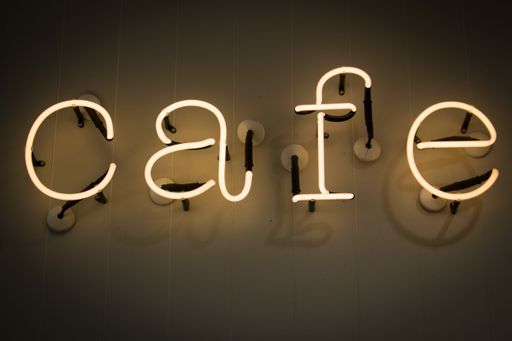 A closeup of a yellow neon sign with the word "cafe"