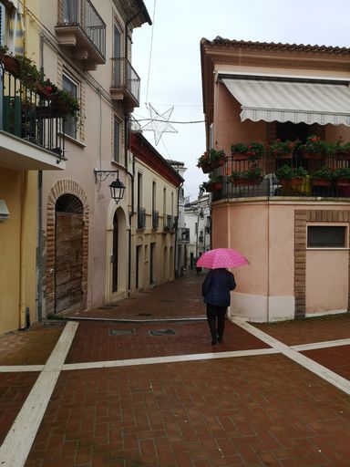 A vertical shot of a lovely street with beautiful buildings and a walking human with a pink umbrella
