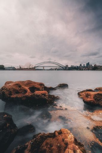 A vertical of a rocky beach against Sydney Opera House on a cloudy day in Australia
