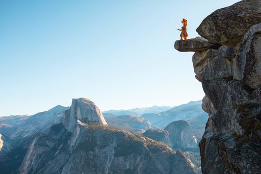 An aerial shot of a person in a dinosaur costume standing at the edge of a cliff and enjoying the view