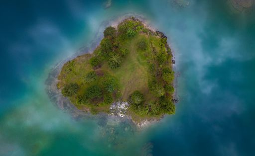 An aerial breathtaking view of a small heart-shaped island surrounded by blue ocean waters
