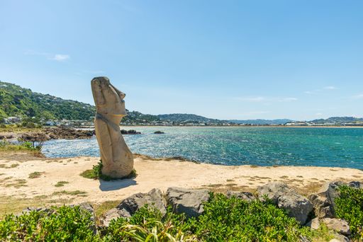 A Moai statue on the sandy coast of Wellington in New Zealand faced the blue sea of Lyall Bay on a sunny day