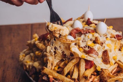 A closeup shot of a dish with french fries, sausages topped with cheese and corn on a wooden table.