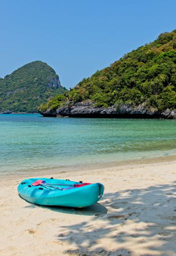 A vertical shot of a blue row boat on the beach by the beautiful ocean and the mountains