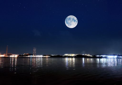 A beautiful full moon in the night sky over a waterscape and urban lights