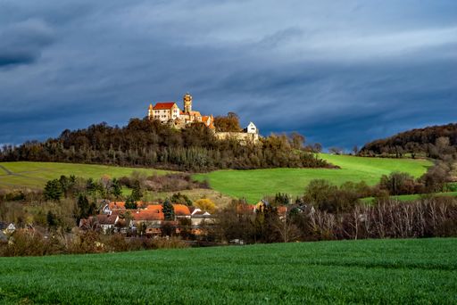 A majestic old castle situated atop a lush green hill, with a rolling expanse of grass in front