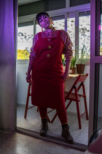 A shallow focus of a young female with short hair wearing a red dress with a shirt and posing in a house