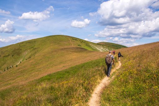 A group of people walking along a narrow trail in the grassy valley. Big Fatra mountains, Slovakia.