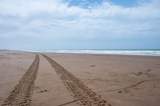 The tire tracks on a sandy beach against a cloudy blue sky