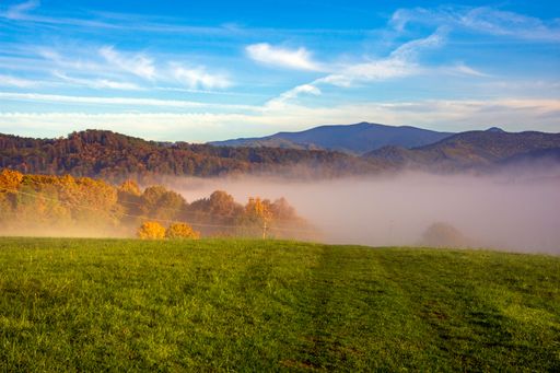 A picturesque landscape of rolling fog over a range of mountains and a green field. Banska Bystrica.