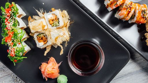 Closeup of a set of sushi rolls on black stone plates served with soy sauce, and wasabi