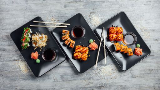 Top view of a set of sushi rolls on three black plates on a gray wooden background