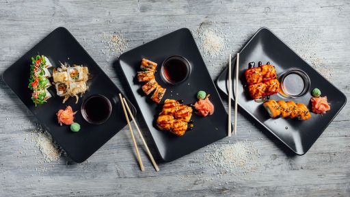 Top view of a set of sushi rolls on three black plates on a gray wooden background