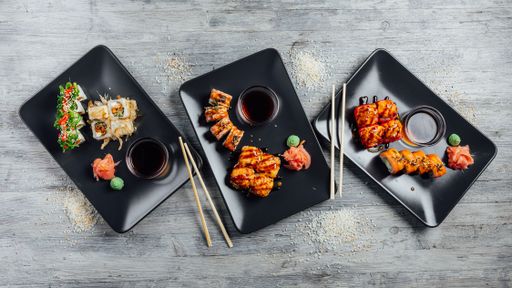 Top view of a set of sushi rolls on three black plates on a gray wooden background