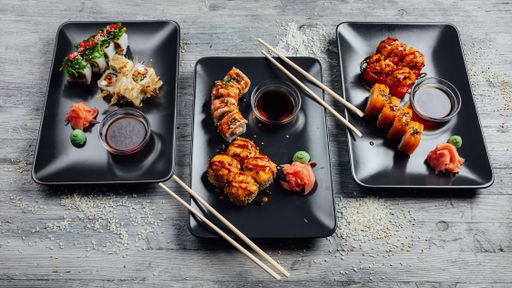 Top view of a set of sushi rolls on three black plates on a gray wooden background