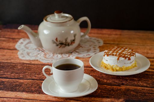 A selective focus shot of a delicious cake with caramel topping and a cup of hot tea