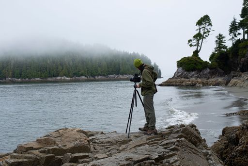 A photographer taking a photo of the mesmerizing nature with the camera on a tripod at the shore in Tofino, British Columbia