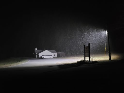 An empty road with snowfall in the light of a street lamp