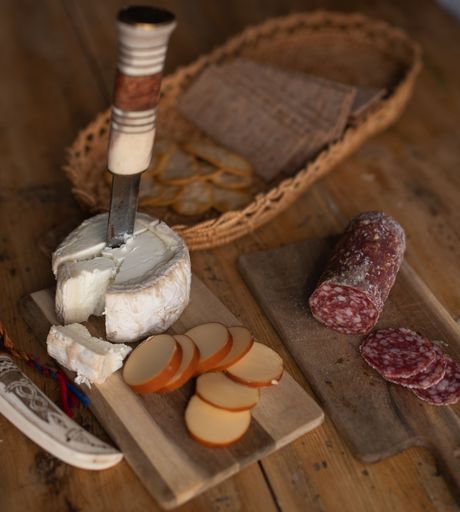 A basket with crackers, two types of cheese and salami over a wooden table