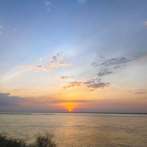 The sun in cloudy sunset sky at a distance over the peaceful lake