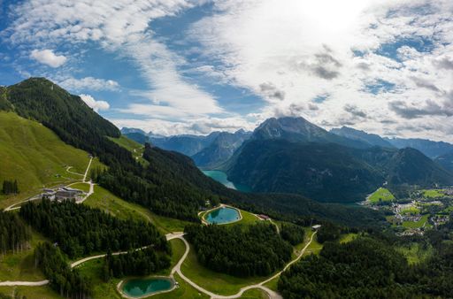 A bird's eye view of lakes in mountains covered with green forests under a cloudy blue sky in Berchtesgaden, Germany
