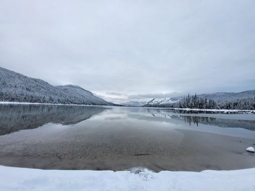 A picturesque view of beautiful mountains covered in snowy trees in the background of a clear lake