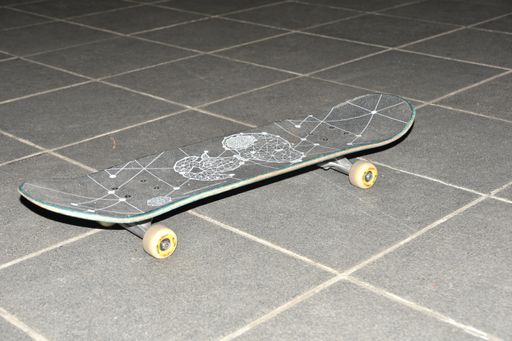 A closeup shot of a decorative skateboard with illustrations on a tiled floor