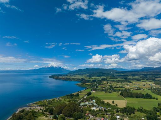 A drone shot of the Osorno Volcano under the blue cloudy sky in Chile with Llanquihue lake on its foot