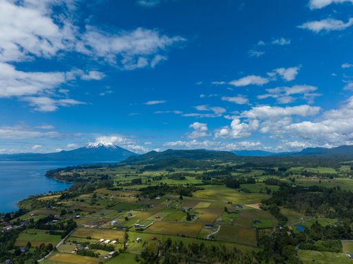 A drone shot of the Osorno Volcano under the blue cloudy sky in Chile with Llanquihue lake on its foot
