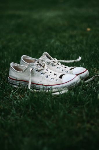 A pair of white Converse sneakers tied together lying in a grassy field, viewed from a top-down perspective
