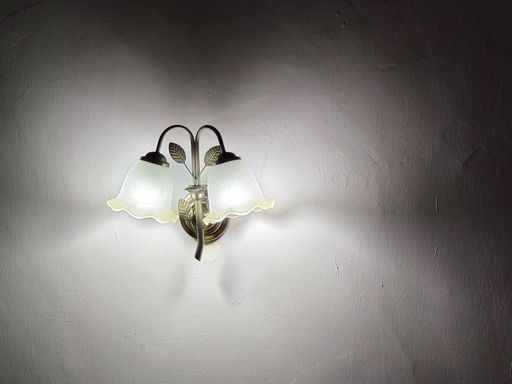 A closeup shot of a vintage chandelier on the wall lamp, casting light on the white wall in the darkroom