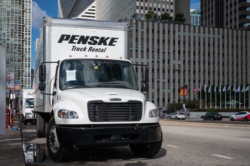A white Penske rental truck on the road in an urban setting