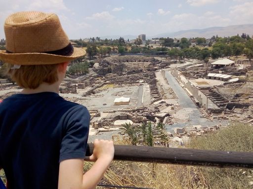 A ginger boy in a straw hat looking at the archeological site in the ancient Beit Shea from a bridge