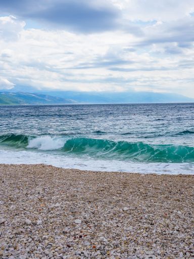A stunning image of Croatia's rugged coastline, featuring waves crashing onto a sandy beach, inlets and rocky outcrops