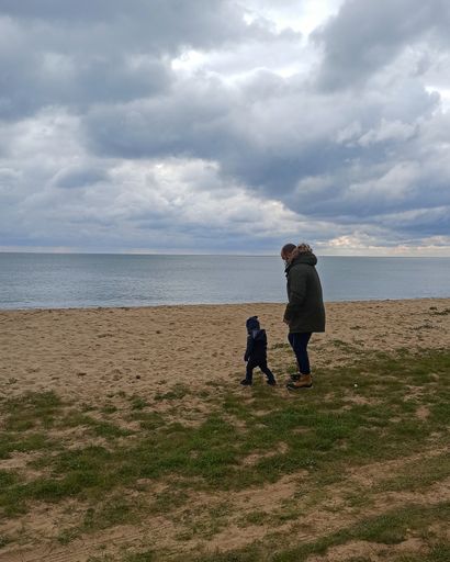 Father and son on a beach with cloudy sky looking out to sea, during the covid-19 pandemic