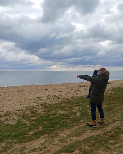 Father and son on a beach with cloudy sky looking out to sea, during the covid-19 pandemic