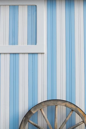 The exterior of a newly painted blue and white striped beach house with an old wheel leaning on it