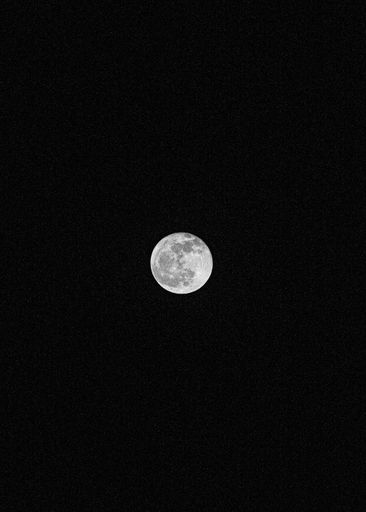 A black-and-white vertical shot of the Moon shining in the sky surrounded by the darkness