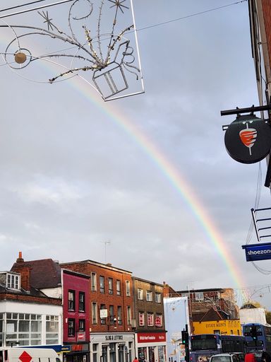 A vertical shot of buildings in Groningen, Netherlands, under the cloudy sky with a rainbow