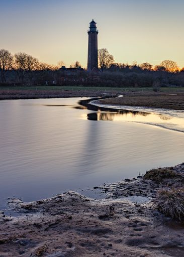 A vertical shot of a river with a brick lighthouse in the background during sunset