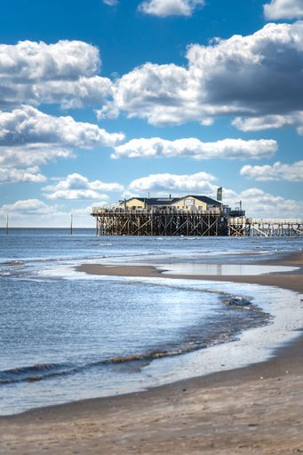 A vertical shot of a building on pier near Baltic sea under white fluffy clouds